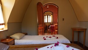 A bedroom with two beds, a wooden chair, a small table, and a door leading to a hallway.