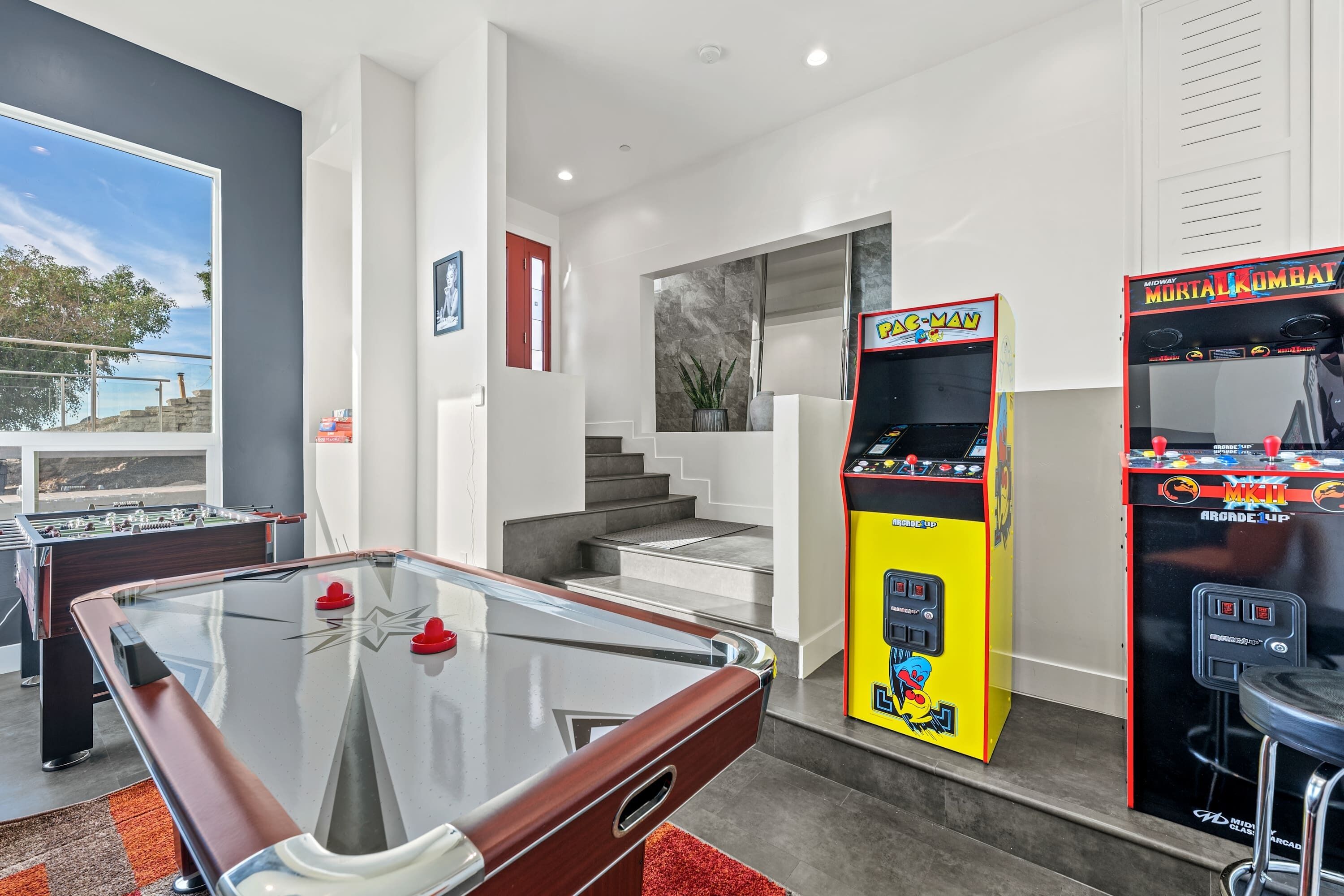 A modern indoor recreational area with a foosball table, two arcade machines, and a pool table.