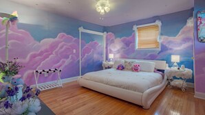 A bedroom with a bed, a nightstand, a dresser, a window with blinds, and a wall mural of clouds. - The Vibrary Inn, a Fantasy Minnewaska Escape. Minutes from Hikes and Waterfalls. (Kerhonkson)