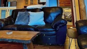 A cozy living room with a leather sofa, a wooden coffee table, and a chandelier. - Stunning Custom Made Log Home- on 30 acres (Grand Forks)