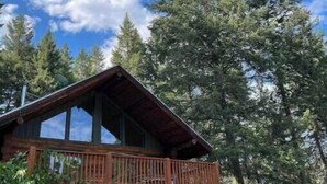 A cabin with a balcony, surrounded by tall trees and a clear blue sky. - Stunning Custom Made Log Home- on 30 acres (Grand Forks)