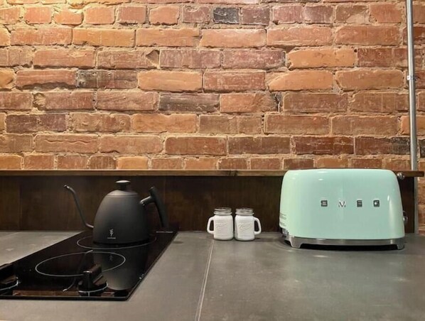 A kitchen with a brick wall, a black electric kettle, a light green toaster, and two white mugs on the counter.