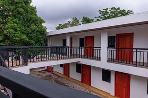Un edificio de dos pisos con balcón, puertas rojas y fachada blanca.