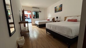 Une chambre d’hôtel avec deux lits, un plancher en bois, une chaise, une poubelle et un tableau au mur.