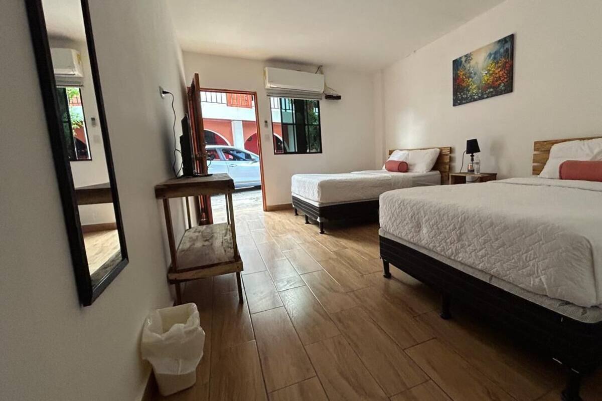 Een hotelkamer met twee bedden, een houten vloer, een stoel, een prullenbak en een schilderij aan de muur.