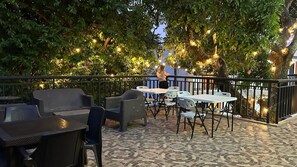 An outdoor patio with tables and chairs, surrounded by trees and string lights.