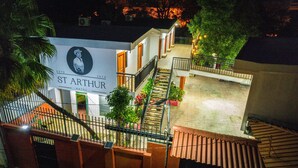 Un hôtel appelé St. Arthur, avec une enseigne représentant un portrait et l’année 2024. Il possède un escalier menant à un balcon agrémenté de plantes et doté d’une balustrade.
