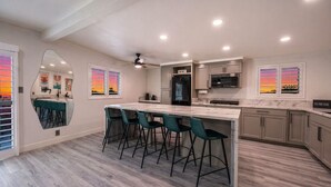 A modern kitchen with a central island, bar stools, a refrigerator, and a microwave. - Licensed 2.5 mi to Strip BBQ Pool Kings (Las Vegas)