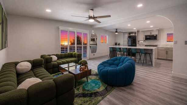 A modern living room with a sectional sofa, a blue bean bag, a glass coffee table, and a view of the sunset through large windows. - Licensed 2.5 mi to Strip BBQ Pool Kings (Las Vegas)