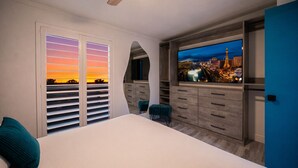 A bedroom with a large bed, a TV, and a view of a cityscape at sunset. - Licensed 2.5 mi to Strip BBQ Pool Kings (Las Vegas)