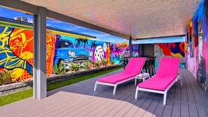 A covered outdoor area with colorful murals, two pink sun loungers, and a wooden deck. - Licensed 2.5 mi to Strip BBQ Pool Kings (Las Vegas)