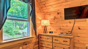 Interior de una cabaña con ventanal, lámpara, reloj y televisor de pantalla plana montado en la pared.