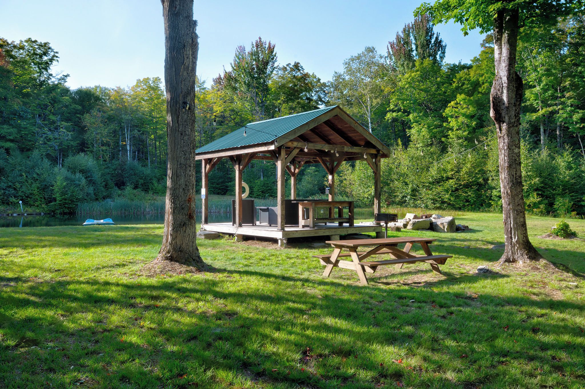 Un belvédère en bois avec un toit vert, des tables de pique-nique et un cadre naturel, comme un parc.