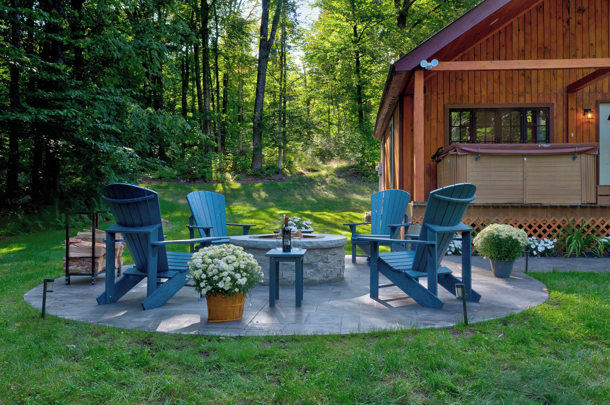 A wooden cabin with a circular outdoor seating area featuring Adirondack chairs and a fire pit.