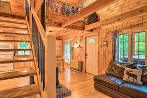 A wooden cabin interior with a staircase, kitchen appliances, a fireplace, and a leather couch.