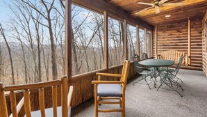Una cabaña de madera con comedor, que incluye una mesa y sillas, ventanas amplias con vistas al bosque y un ventilador de techo.
