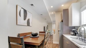 A modern kitchen with a dining area, featuring a wooden table, chairs, a refrigerator, and a sink.