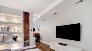 A modern living room with a round coffee table, a sofa, a TV mounted on the wall, and a brick accent wall.