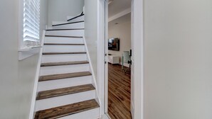 A staircase with wooden steps and white walls, leading to a room with a wooden floor and a flat-screen TV mounted on the wall.