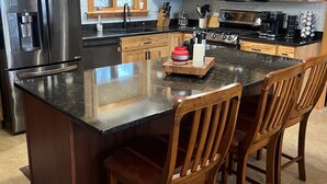 Een moderne keuken met houten kastjes, roestvrijstalen apparatuur en een centraal eiland met barkrukken.