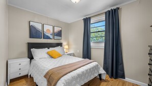 A bedroom with a bed, nightstands, a window with curtains, and artwork on the wall.