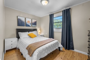 A bedroom with a bed, nightstands, a window with curtains, and artwork on the wall.