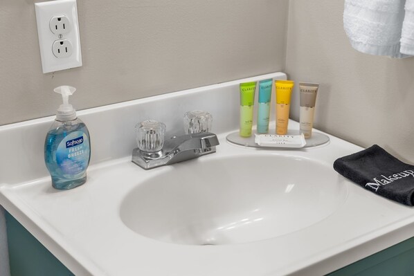A bathroom sink with a bottle of Softsoap Fresh Breeze, three glass soap dispensers, and a row of Clariti skincare products.