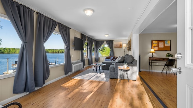 A spacious living area with a large window overlooking a body of water, a sofa, a coffee table, and a desk with a lamp.