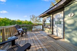 A wooden deck with two lounge chairs and a table, overlooking a body of water.