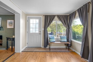A room with a wooden floor, a bench with pillows, a door, and large windows with curtains.