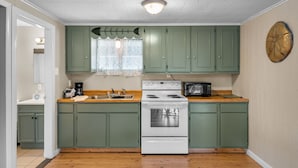A compact kitchen with green cabinets, a white stove, a microwave, and a wooden countertop.