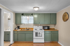 A compact kitchen with green cabinets, a white stove, a microwave, and a wooden countertop.