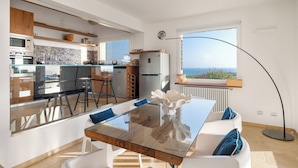 Eine moderne Küche mit Meerblick, ein Essbereich mit einem Glastisch und ein großes Fenster mit Aussicht.