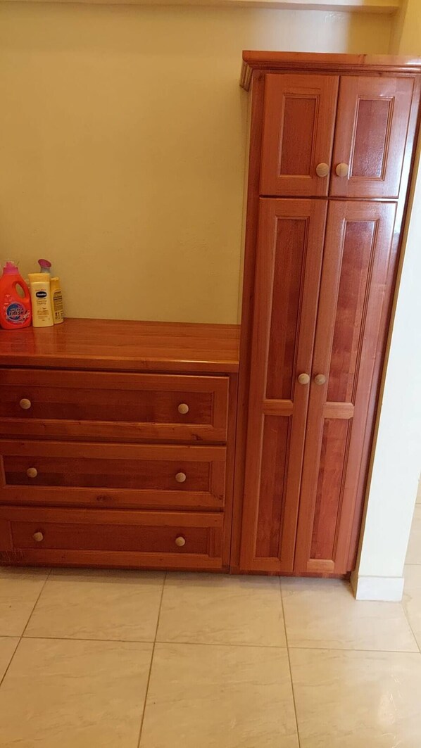 A wooden cabinet with drawers and a door, placed against a wall with a tiled floor.