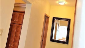 Un couloir avec une porte en bois, un miroir encadré et un luminaire au plafond.