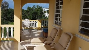 Un espace de détente extérieur baigné de lumière, avec des fauteuils blancs et une vue sur la végétation environnante.