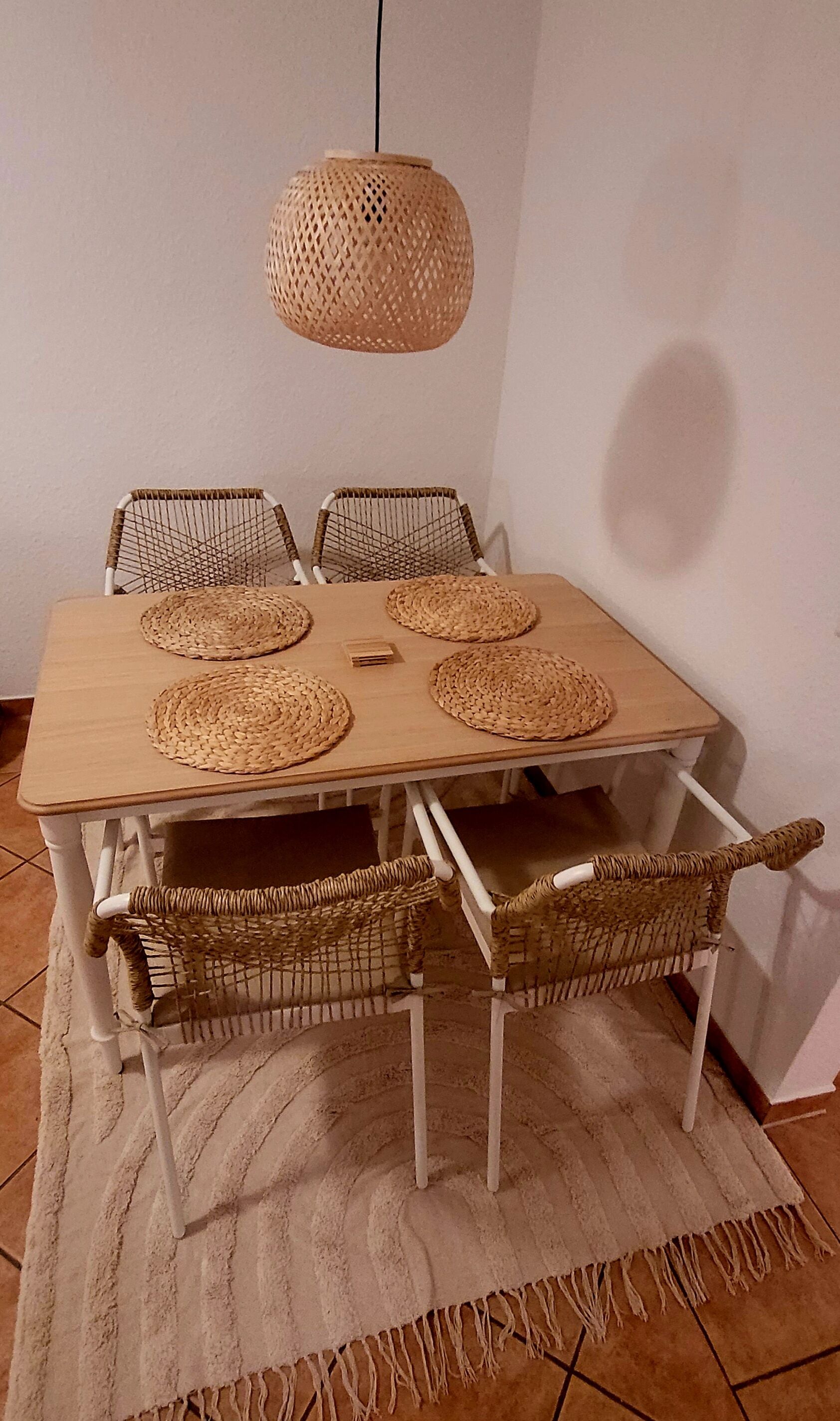 Spisebord med vævede bordskåner, fletstole og en hængende lampe.