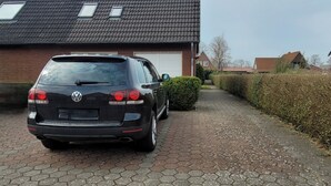 A black Volkswagen parked on a paved driveway leading to a house with a tiled roof and a garage. - Luette Ostfreesenstuuv (Holtgast)
