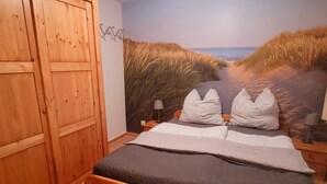 A bedroom with a bed, wooden wardrobe, and a beach mural on the wall. - Luette Ostfreesenstuuv (Holtgast)
