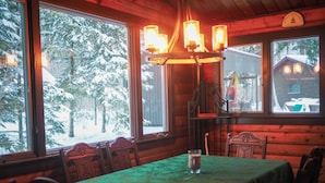 En mysig stuga med ett matbord, stolar och en kristallkrona. Stora fönster ger utsikt över en snötäckt skog.