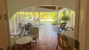Un patio con ventilador de techo, asientos exteriores y vista a un jardín.