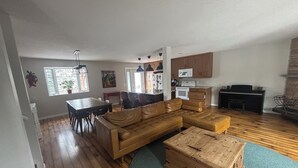 A spacious living room with a large sectional sofa, a dining area with a table and chairs, a kitchen with wooden cabinets and appliances, and a fireplace. - Cozy Calgary Stampede Sanctuary Home (Calgary)