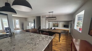 A spacious kitchen with a large island, wooden flooring, pendant lighting, and a view of the dining area. - Cozy Calgary Stampede Sanctuary Home (Calgary)