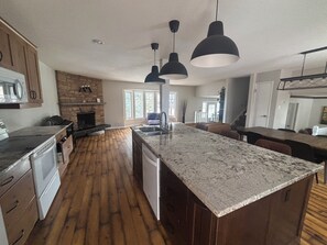 A modern kitchen with a large island, wooden flooring, and pendant lighting. - Cozy Calgary Stampede Sanctuary Home (Calgary)