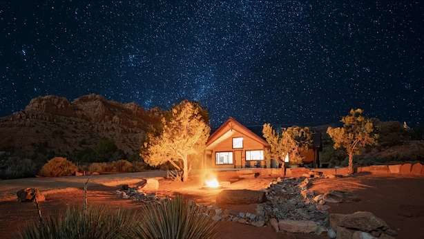 Una casa con un brasero en el frente, rodeada de rocas y plantas del desierto, bajo un cielo estrellado.