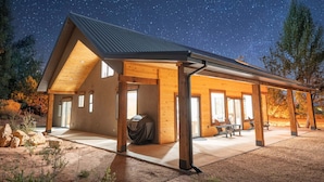 Un lodge moderno y espacioso con un espacio al aire libre cubierto y ventanas amplias, frente a un cielo nocturno estrellado.