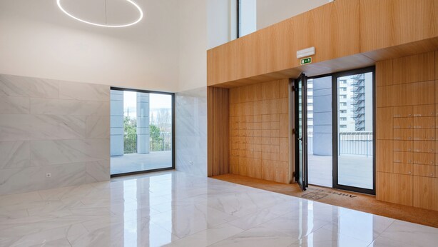 Un hall d’entrée moderne avec un sol en marbre, des lambris en bois, une porte vitrée donnant sur l’extérieur et un luminaire circulaire au plafond.