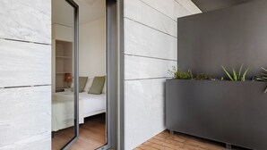 Une chambre moderne dotée d’une porte coulissante donnant sur une chambre à coucher, d’un pot de fleurs gris contenant des plantes et d’un plancher en bois.