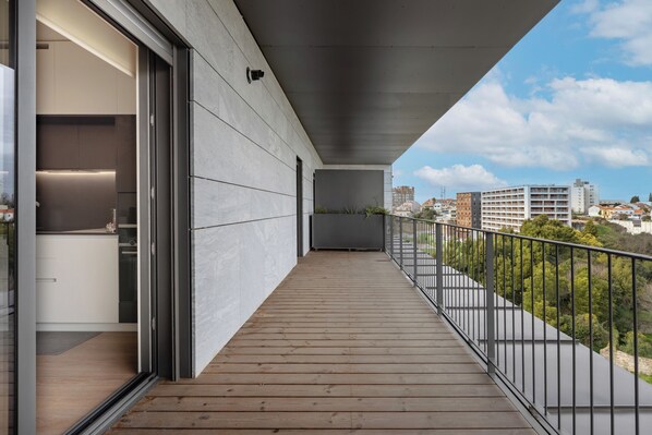 A balcony with a wooden floor, metal railing, and a city view. - Antas Green Executive (Porto)