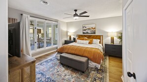 A bedroom with a bed, nightstands, a ceiling fan, a large window, and a view of the outdoors. - Tailgaters paradise, grill, game room, sunroom-large backyard! (Columbia)